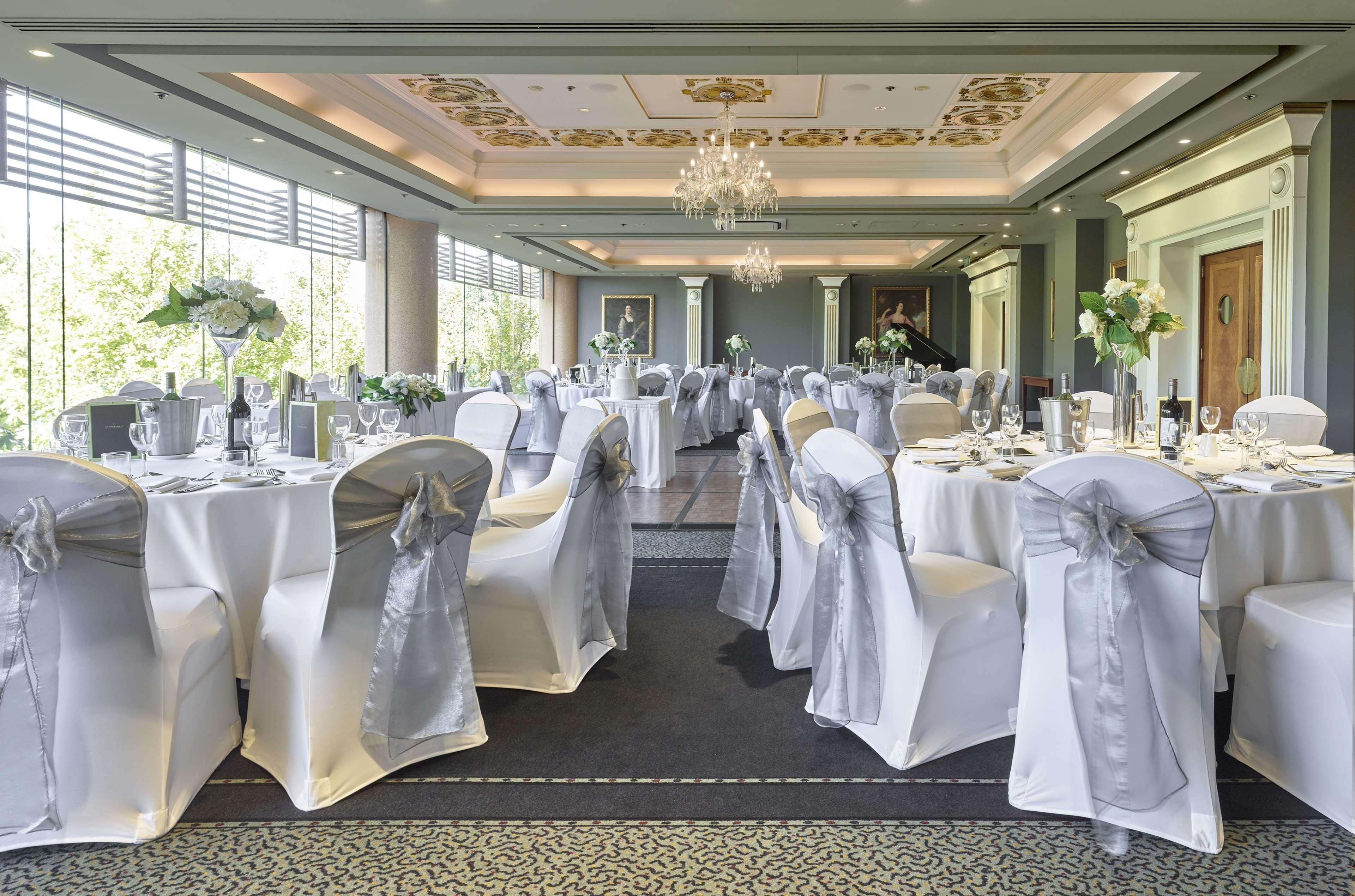 Hotel Stamford Plaza Adelajda Zewnętrze zdjęcie The photo displays an elegantly arranged banquet hall. The room features several round tables covered with white tablecloths, each adorned with silver sashes on the chairs. There are floral centerpieces, possibly white flowers, on the tables, adding 