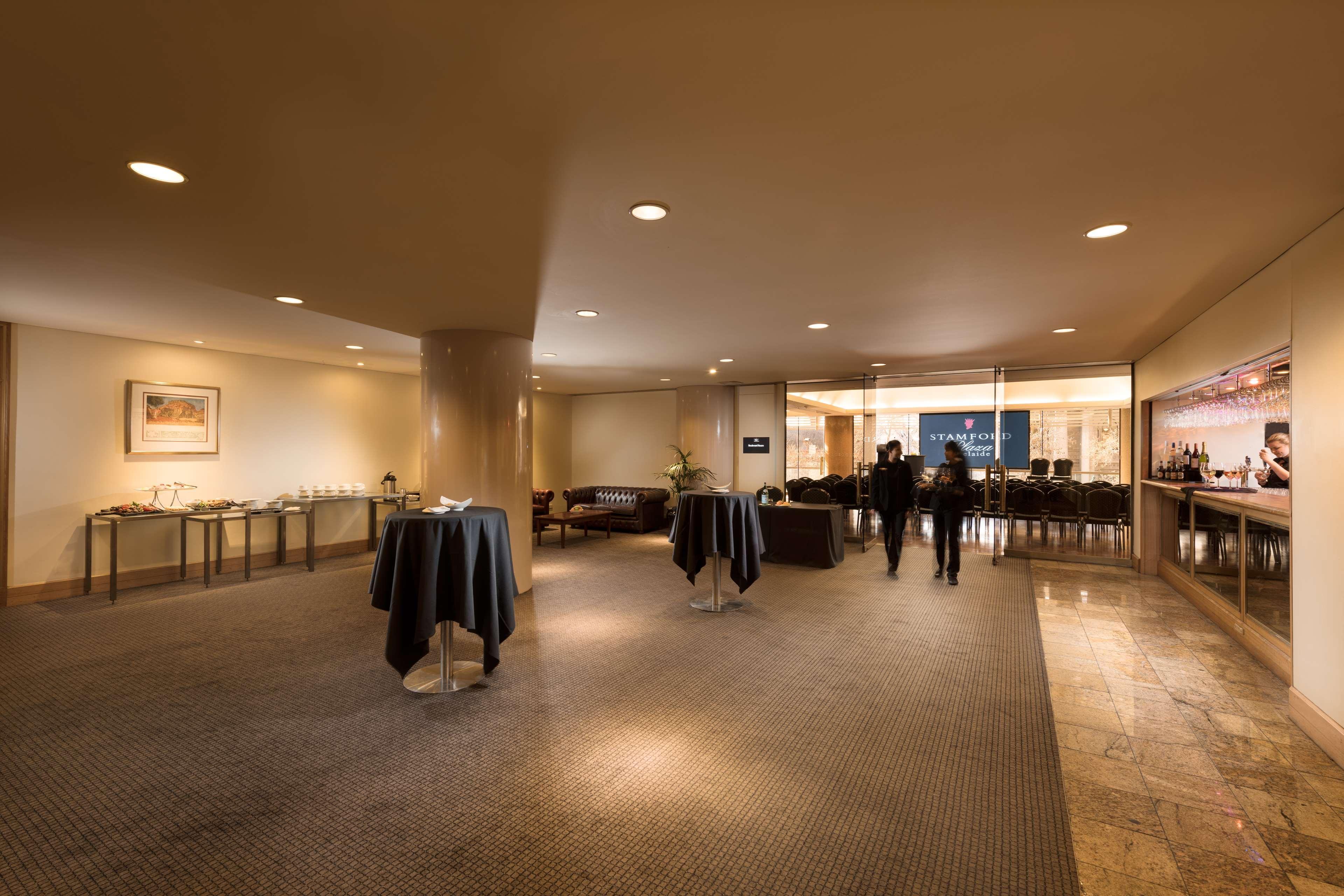 Hotel Stamford Plaza Adelajda Zewnętrze zdjęcie The image shows an indoor space that appears to be a lounge or reception area. There are several round tables with dark tablecloths positioned throughout the room. The floor is carpeted, and the lighting is warm and somewhat dim. In the background, t