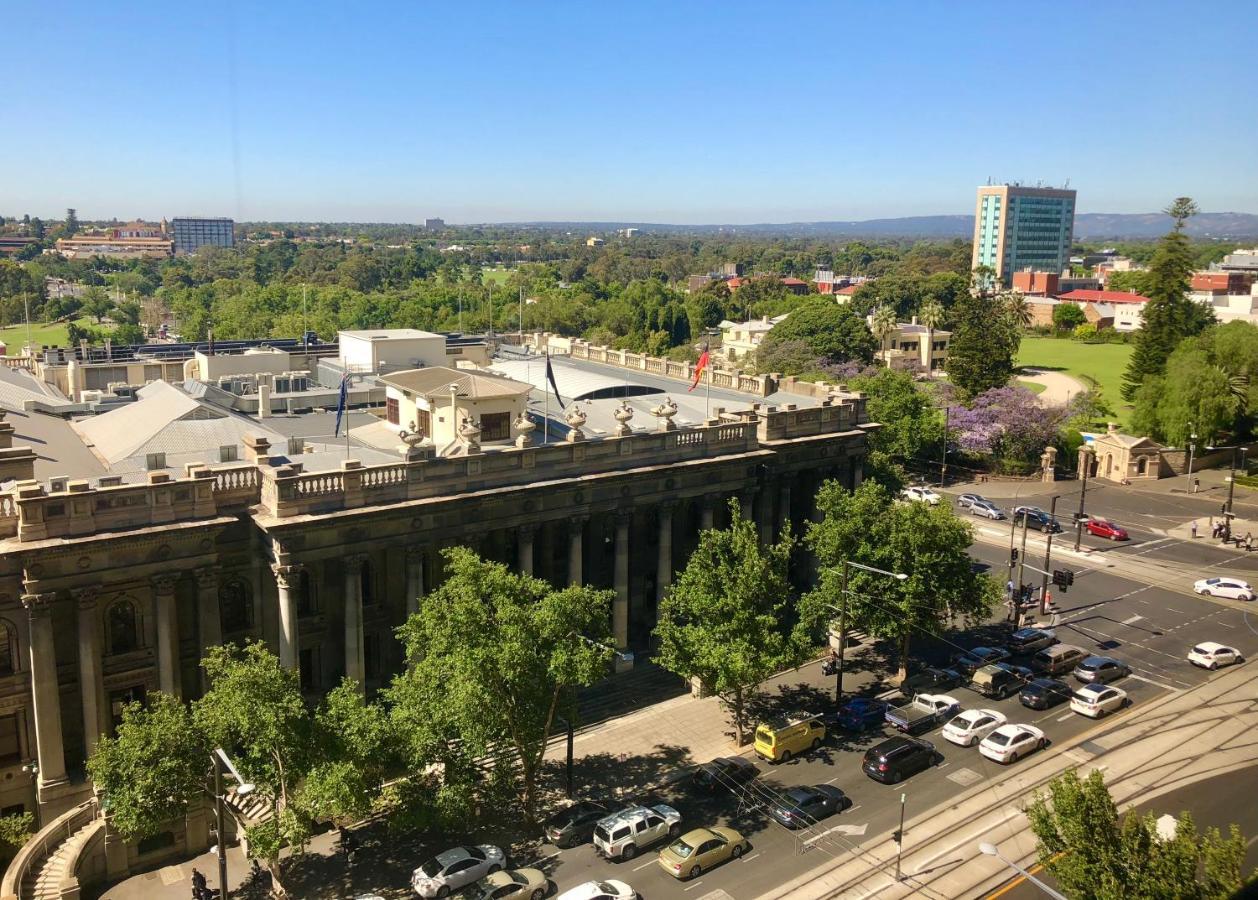 Hotel Stamford Plaza Adelajda Zewnętrze zdjęcie The photo depicts a cityscape view, showcasing a mix of architectural structures and greenery. In the foreground, there is a large, classical building with columns, suggesting it may be a historical or governmental structure. Surrounding the building